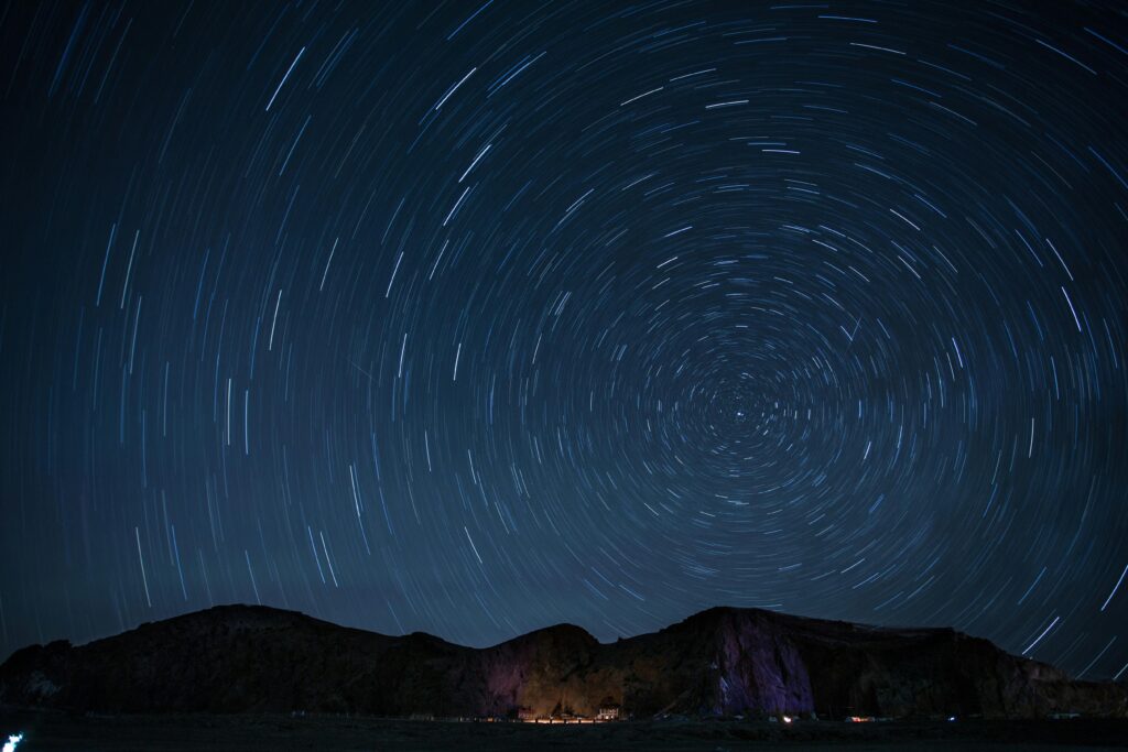 A mesmerizing night sky showcasing rotating star trails over a mountainous landscape.